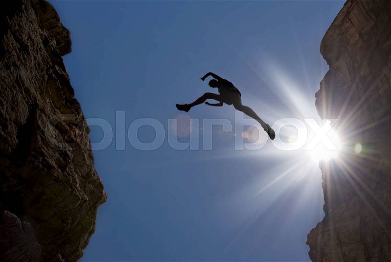 Man jumping over precipice between two mountains, stock photo