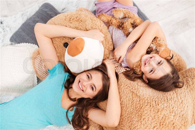 Cheerful cute sisters lying on soft plush bear at home, stock photo