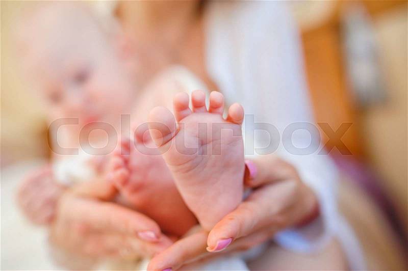 Happy young mother holding little feet of her son, stock photo