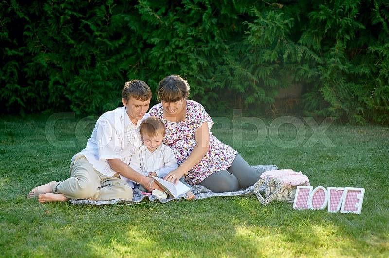 Family sitting on the grass in a park with letters love and read book, stock photo