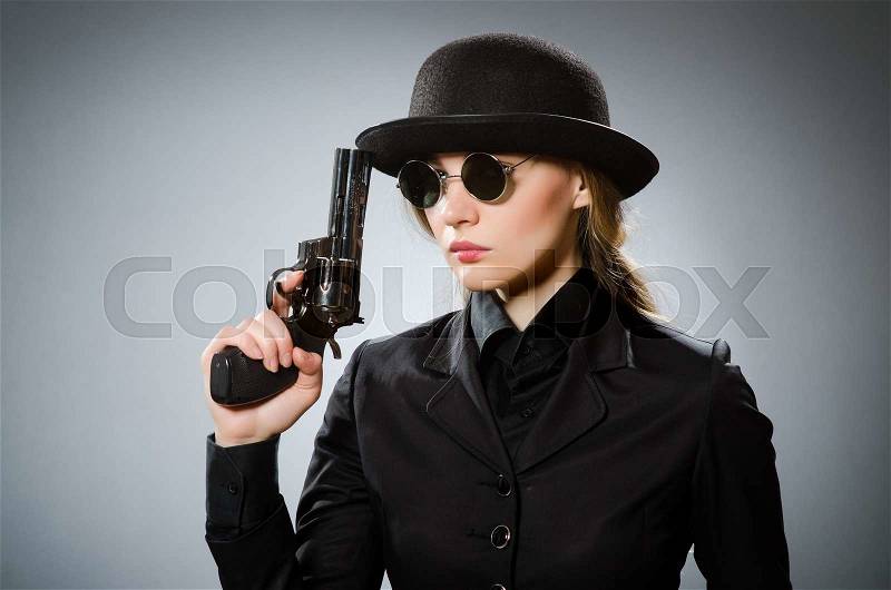 Female spy with weapon against gray, stock photo