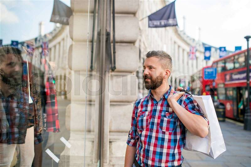 Young hipster man in checked shirt shopping, holding a bag, in the streets of London, doble decker buss, stock photo