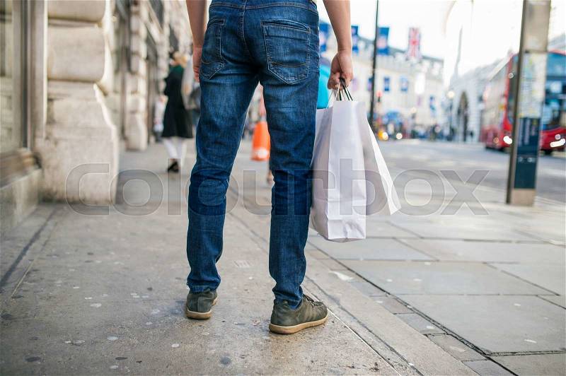 Legs of unrecognizable man with shopping bags in the crowded street of London, back view, rear viewpoint, stock photo