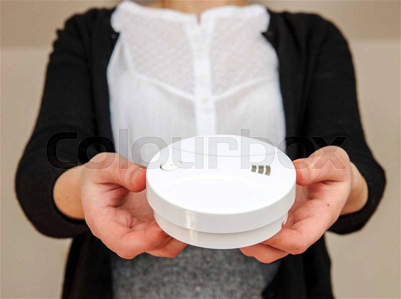 Woman holding white smoke detector - the device that senses smoke, typically as an indicator of fire, stock photo