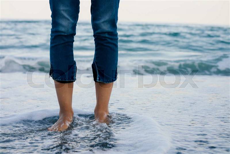 Woman legs in blue jeans standing in the sea water on the coast, stock photo