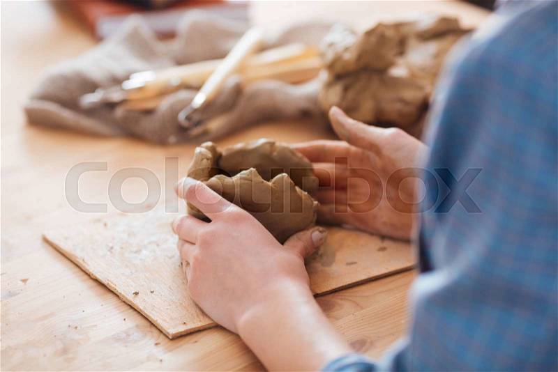 Closeu of woman eramist hands working on sculpture on wooden table in workshop, stock photo