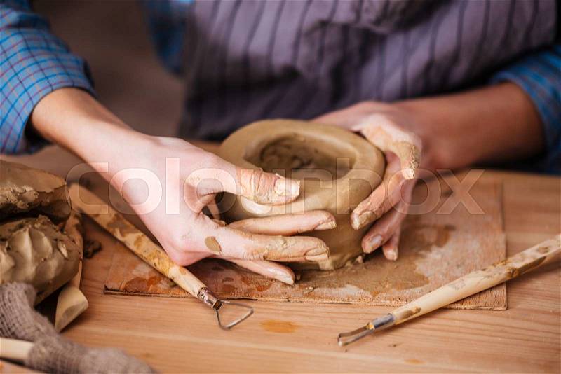 Closeup of clay pot making by hands of young woman in pottery workshop, stock photo