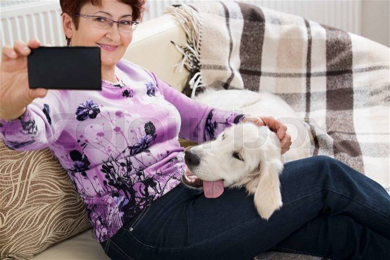 Modern senior woman with her pet shooting selfie picture by phone, stock photo