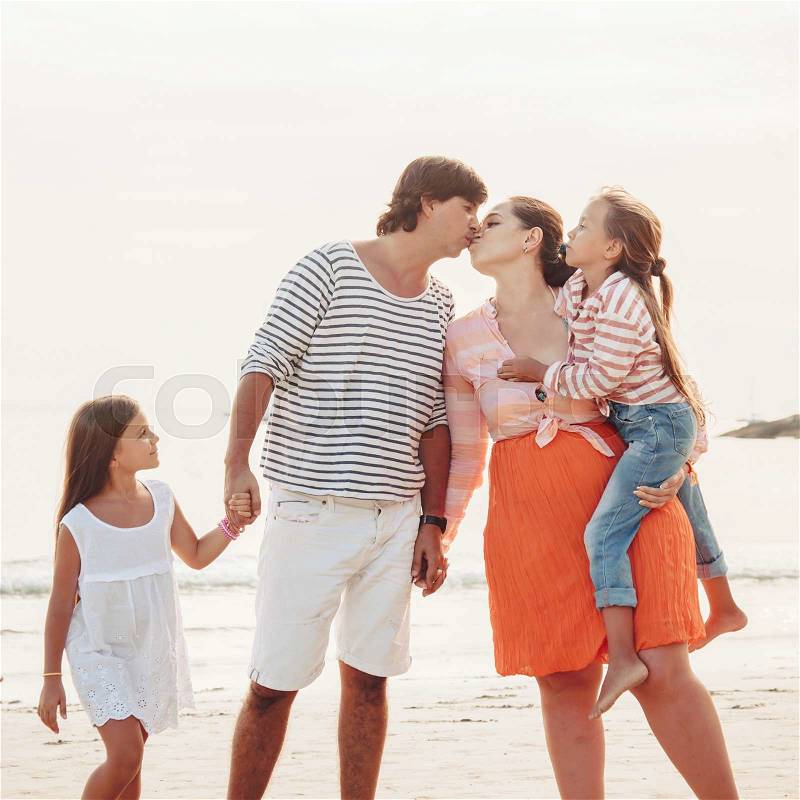 Family walking on the evening beach during sunset, travel photo series. Parents holding hands and kissing, stock photo