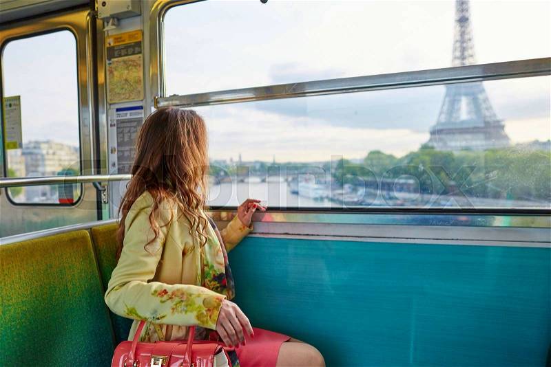 Beautiful young woman travelling in a train of Parisian underground and looking through the window at the Eiffel tower, stock photo