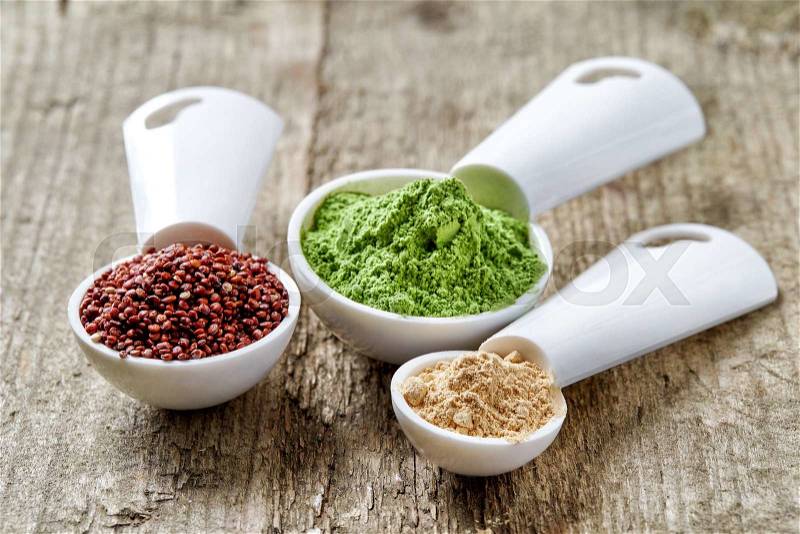 Measuring scoops with barley or wheat grass powder, red quinoa and maca powder on wooden table, stock photo