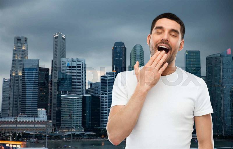 Rest, bedtime and people concept - tired yawning man over evening singapore city background, stock photo