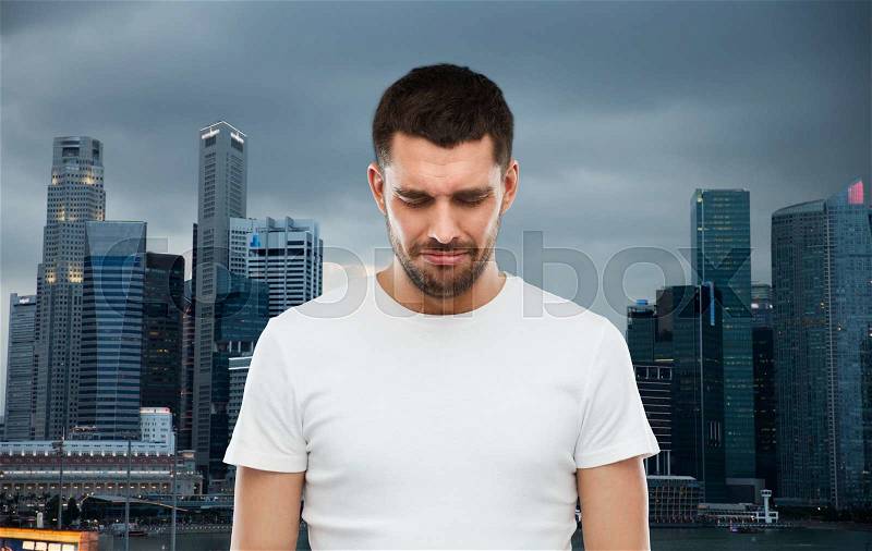 Emotion, sadness and people concept - unhappy young man over evening singapore city background, stock photo