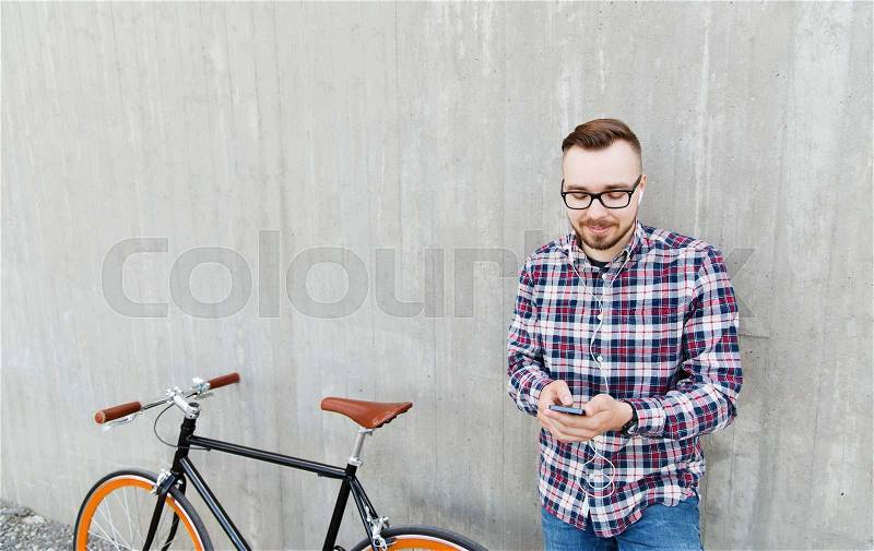 People, style, technology, leisure and lifestyle - happy young hipster man in earphones with smartphone and fixed gear bike listening to music on city street, stock photo
