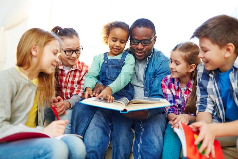 Group of pupils and their teacher reading together, stock photo