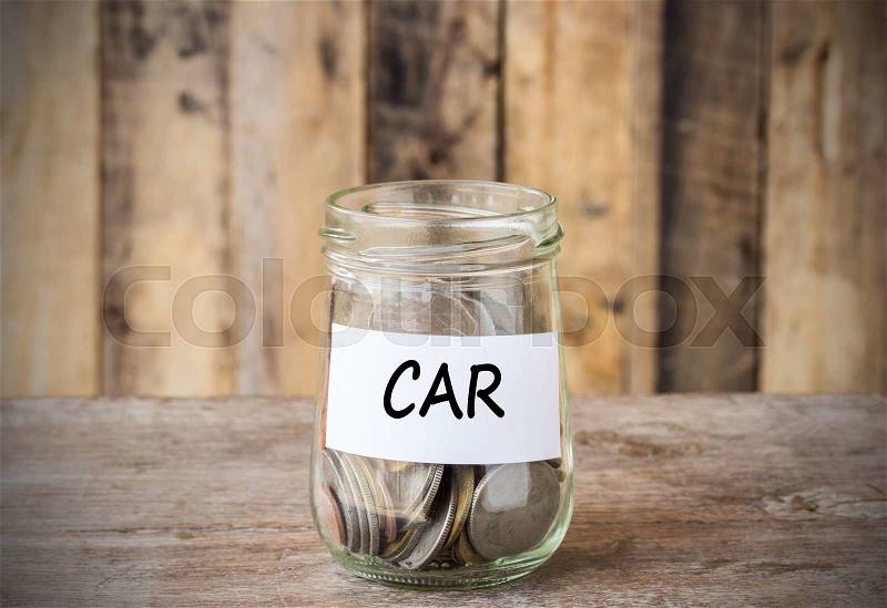 Coins in glass money jar with car label, financial concept. Vintage wooden background, stock photo