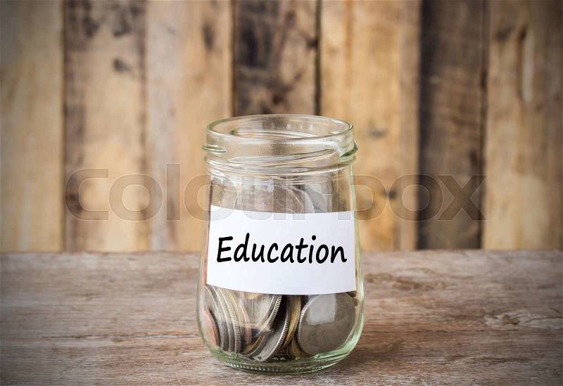Coins in glass money jar with education label, financial concept. Vintage wooden background, stock photo