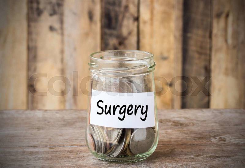 Coins in glass money jar with surgery label, financial concept. Vintage wooden background, stock photo