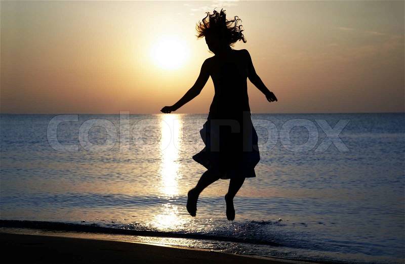 Silhouette of the happy woman jumping and dancing at the sea during sunset. Natural light and shadows, stock photo