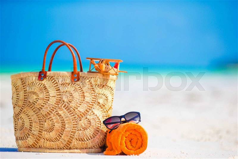 Beach accessories - toy plane, straw bag, orange towel and unglasses on the beach, stock photo