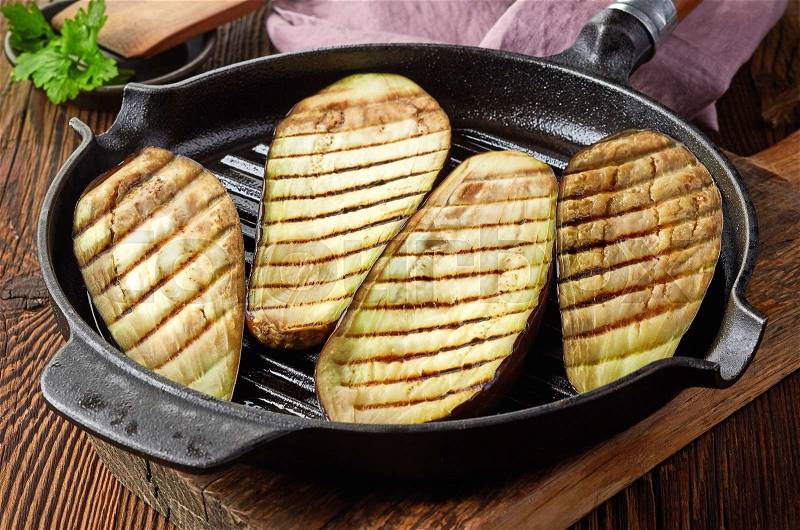 Grilled eggplants on cooking pan on wooden table, stock photo