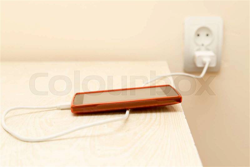 Cell phone is being charged from the electrical outlet, stock photo