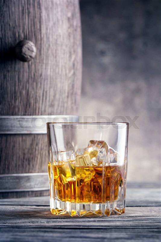 Round glass of whiskey with ice cubes against the background of wooden barrels, stock photo