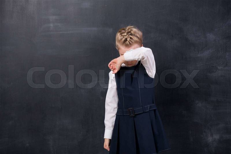 Offended little schoolgirl standing at the blackboard and crying, stock photo