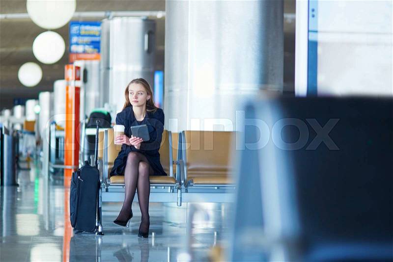 Young woman in international airport, reading and drinking coffee while waiting for her flight, stock photo