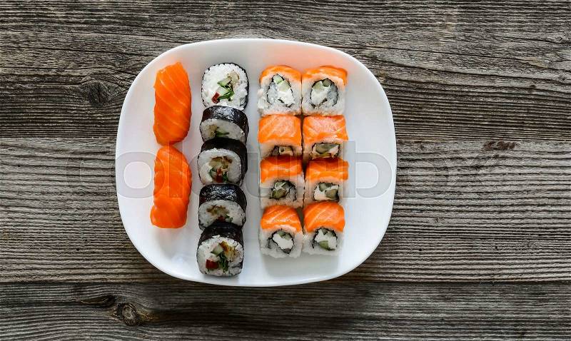 Various sushi on white plate on wooden background, stock photo
