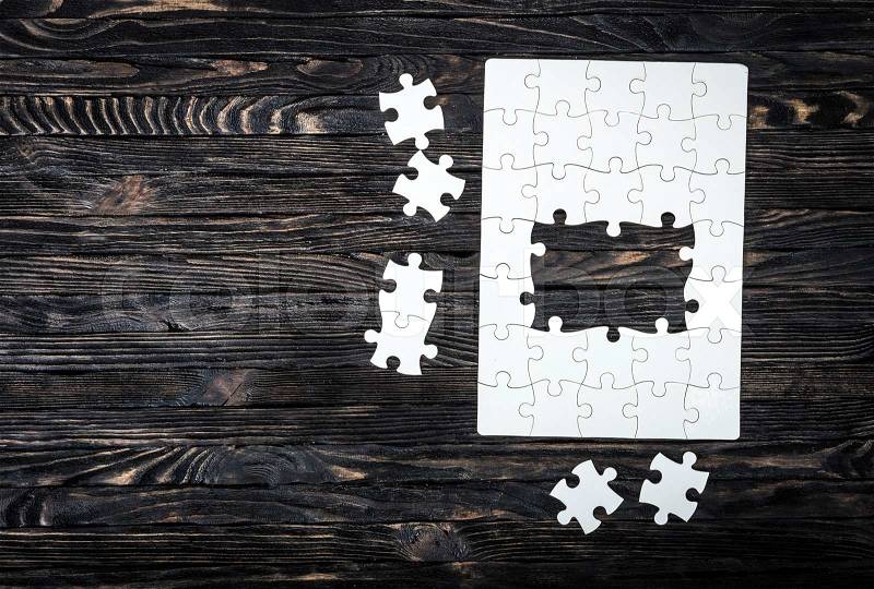 Started puzzle with uncompleted center and pieces on dark wooden background, stock photo