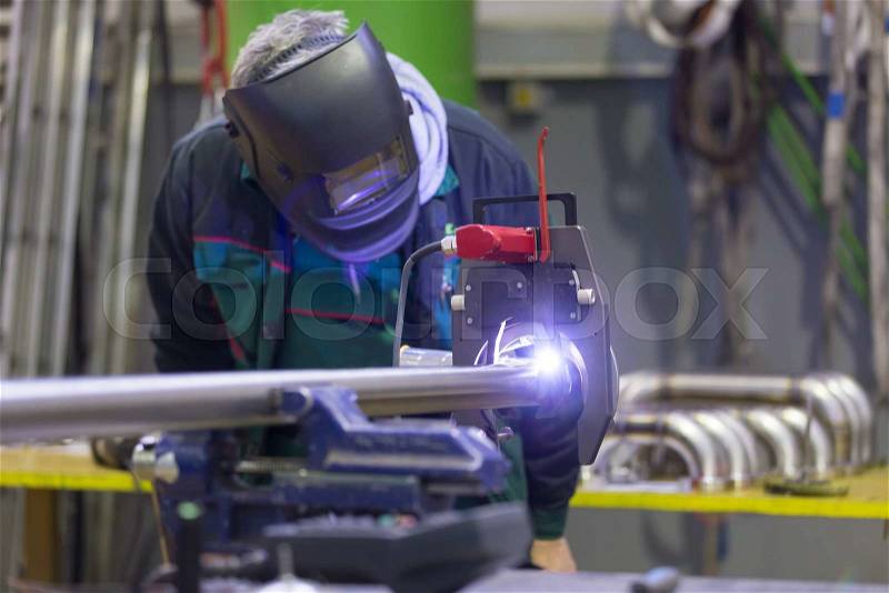 Industrial operator setting computer controlled process of orbital welding machine in inox pipes manufacturing workshop, stock photo
