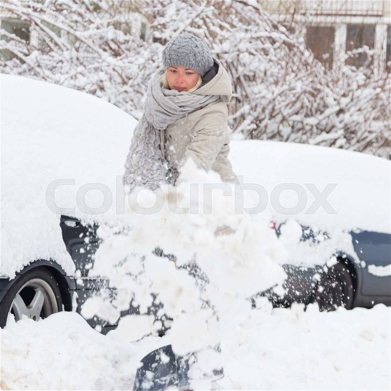 Independent woman shoveling her parking lot after a winter snowstorm, stock photo