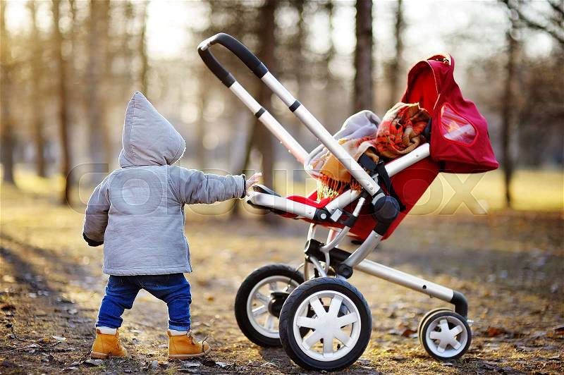 Toddler boy playing with his stroller walking outdoors at the warm spring day, stock photo