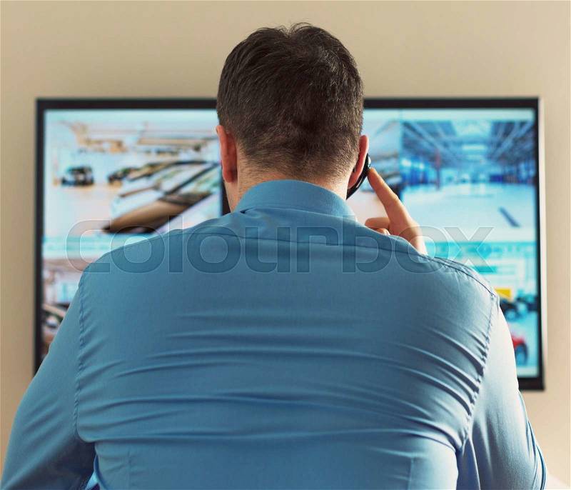 Security guard monitoring video in security room. From the back, stock photo