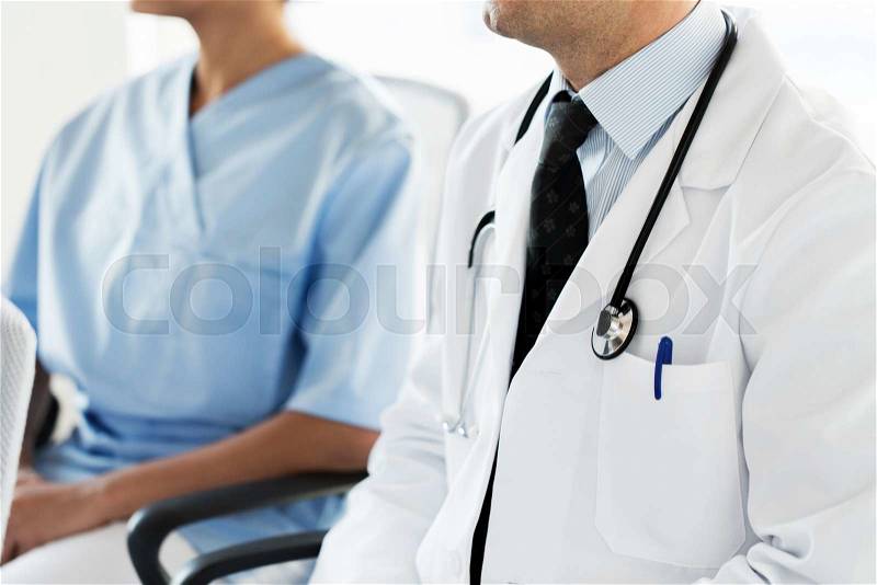 Education, profession, people and medicine concept - close up of happy doctors at seminar or conference in hospital, stock photo