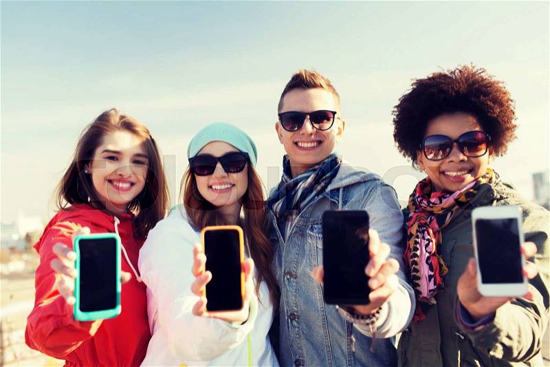 People, friendship, cloud computing, advertising and technology concept - group of smiling teenage friends showing blank smartphone screens outdoors, stock photo