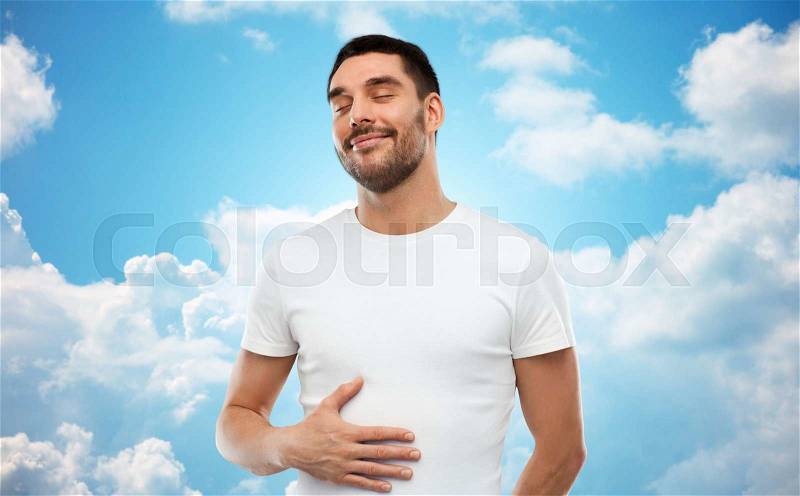 Satisfaction, healthy eating and people concept - happy full man touching his tummy over blue sky and clouds background, stock photo