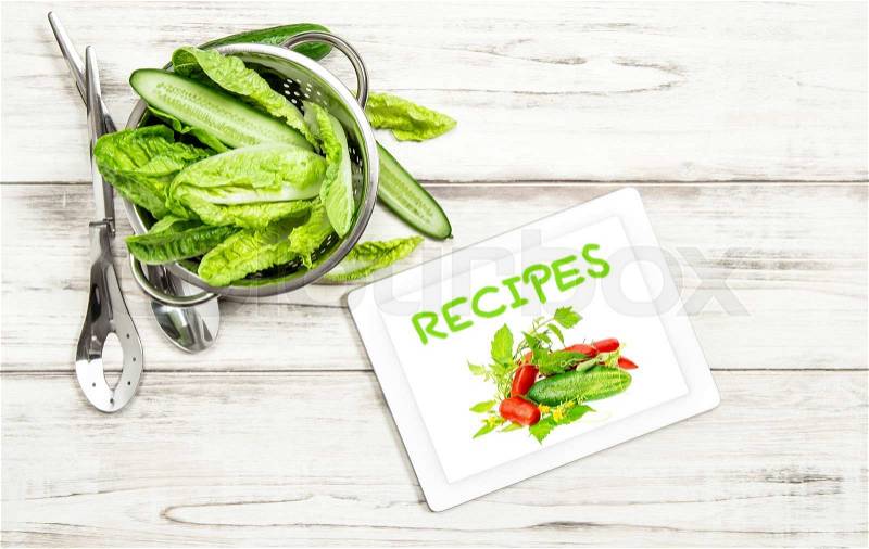 Green salad vegetables with recipe book tablet pc on kitchen table. Internet cook book concept, stock photo