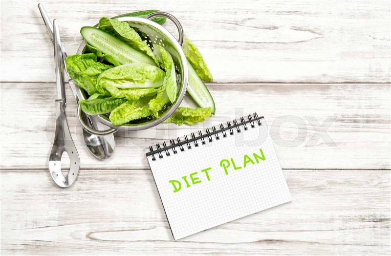 Green salad leaves and vegetables with diet plan journal on white wood kitchen table. Healthy food concept, stock photo