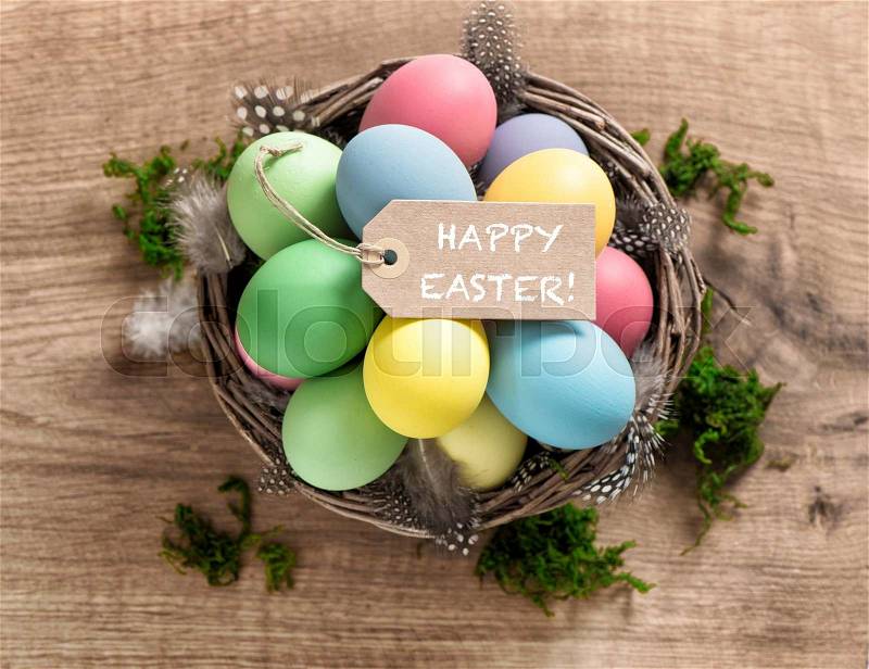 Easter eggs with feather decoration and tag on wooden background, stock photo