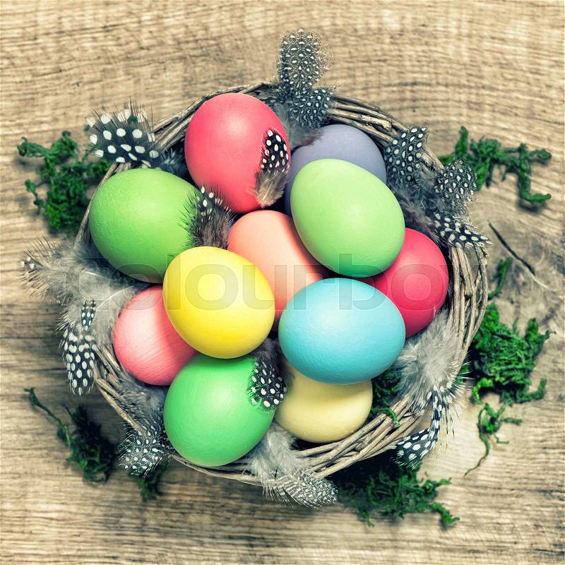 Easter eggs with feather decoration in basket on wooden background. Vintage style toned picture, stock photo