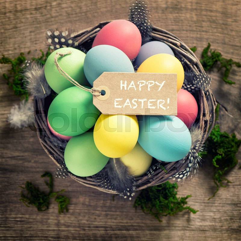 Easter eggs with feather decoration and tag on wooden background. Vintage style toned picture, stock photo