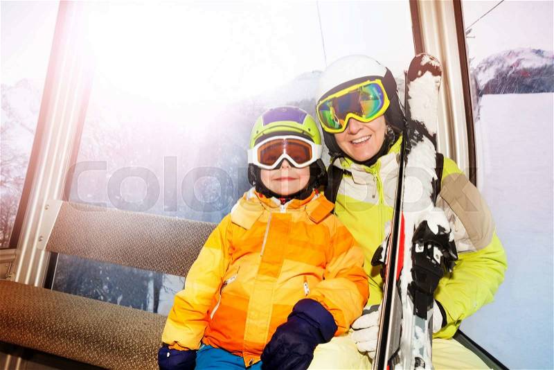 Child and mother sit in cablecar lifting on top of the mountain with ski and smiling , stock photo