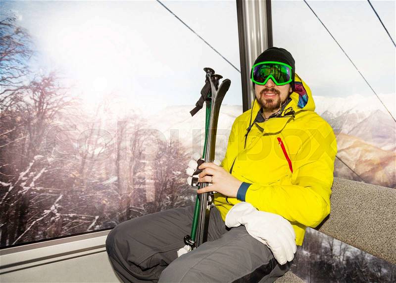 Man skier with beard and wearing ski mask sit in ski lift cable car cabin, stock photo