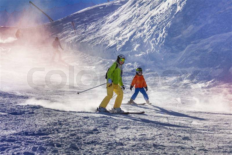 Mom and child ski down the piste teaching how to go down with sunlight lit through snow mist, stock photo