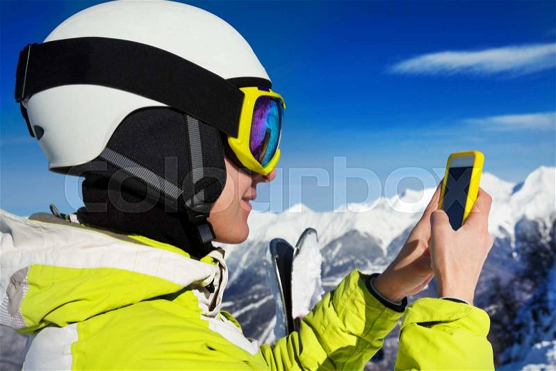 Young skier woman look up something in the phone wearing ski mask and helmet view over the shoulder, stock photo