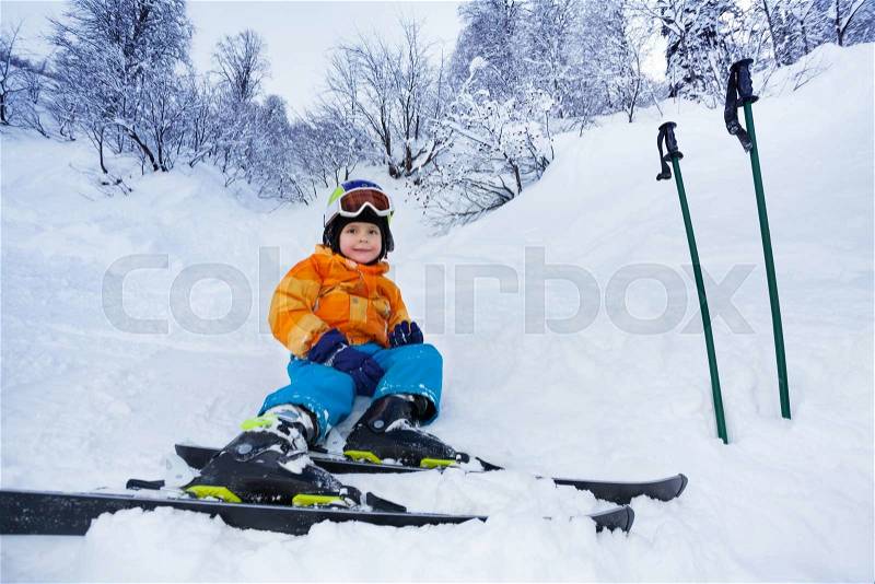 Little skier boy sit in snow resting after ski school lesson, stock photo