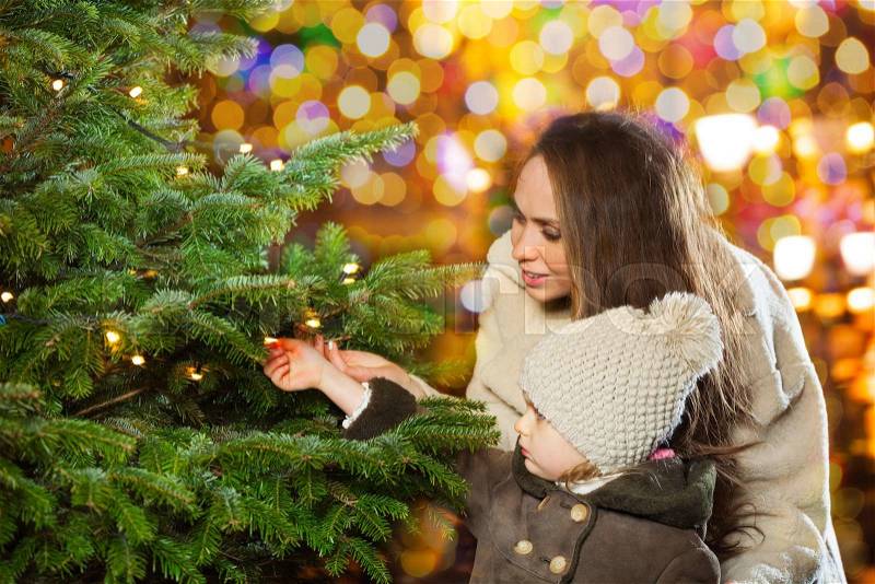 Little girl and her mother have a good time in the city park looking at new year tree in illuminated city, stock photo