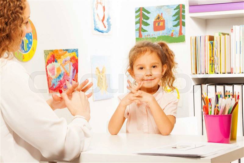 Teacher showing finger exercises to pupil at the table in bright classroom, stock photo